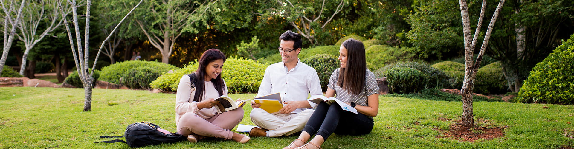 Three people reading books together in a park setting.