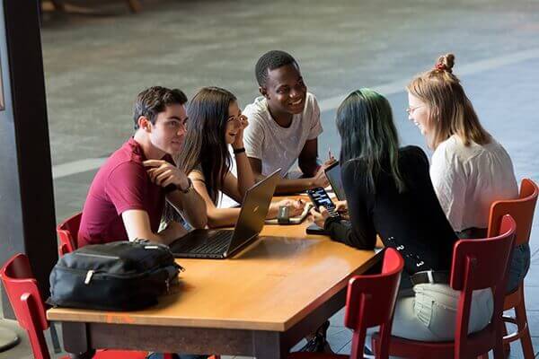 Group of students engaged in discussion around a laptop at a table.