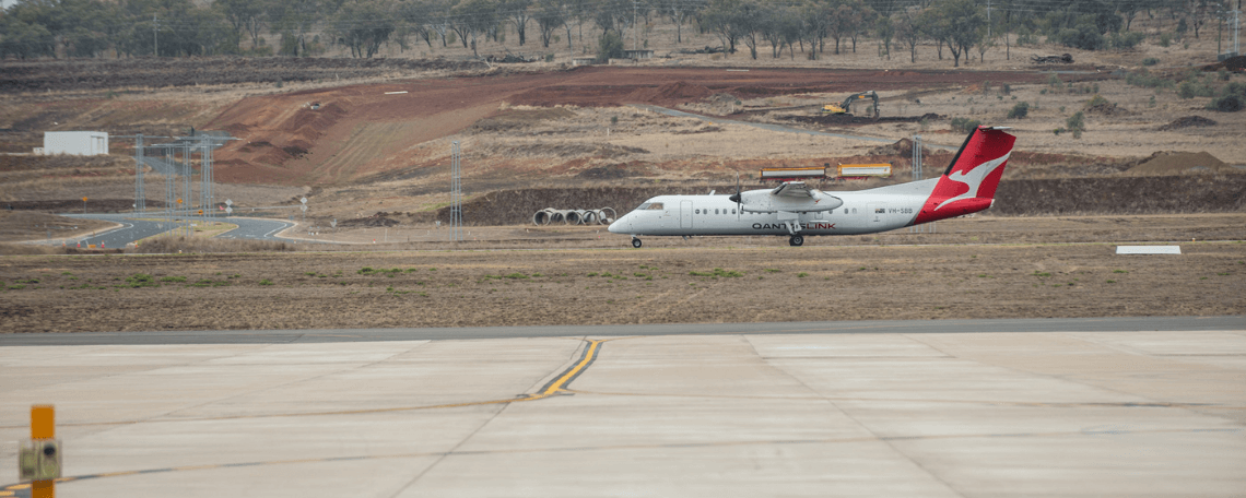 A Qantas Link airplane on a runway with construction work in the background.